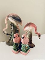 Photo showing two ceramic flamingo figurines and two small flamingo salt and pepper shakers arranged on a flat surface.