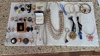 Full lot showing rings, earrings, necklaces, bracelets, pendants, charms, and scarf hooks laid out on a white towel on a table.