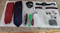 All items laid out on white cloth: 2 ties, 3 wristwatches (Casio and Swiss Military), 3 pocket tools, 3 pairs of cufflinks, and 1 belt buckle.