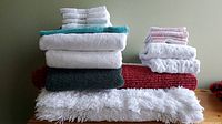 Stack of assorted towels and mats in white, black, turquoise, burgundy, and pink colors showing variety of textures and sizes.