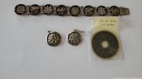 Bracelet, earrings, and Chinese dragon coin pendant arranged on white background.