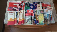 Overview of the entire collection of vintage gas station maps stacked spread out on a table, showing a variety of colorful fold-out and booklet style maps.
