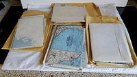 Multiple stacks of folded vintage maps wrapped partially in yellowed protective paper on a flat surface.