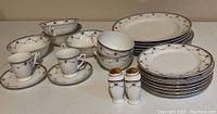 Display of several plates, cups, saucers, and two salt and pepper shakers all decorated in black and gold patterns on white china.