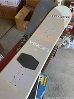 Three snowboards stacked, top one is Sevendust Vision 150 model, light grey color with black traction pad.