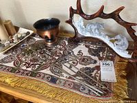 Full overview of statue, vessel, skewers, and dish on table runner