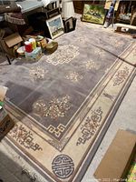 Full view of large Chinese style rug on floor surrounded by assorted household items.