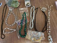 Top view of all necklaces spread out showing black, silver-tone, green beads, clear crystals, and a decorative brooch.