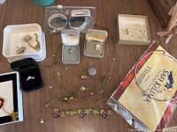 Overview photo showing many pieces of costume jewelry including necklaces, bracelets, and rings on a wooden surface with some in small boxes or bags.