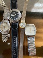 Eight wrist watches of assorted styles on a reflective surface showing metal link bands, leather straps, and novelty character watch.
