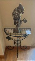 Metal parrot statue placed on a metal stand, showing full front view.