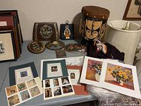 Overview of museum art prints, leather art plaques, framed vintage art, and decorative pieces arranged flat on table