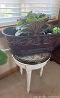 View of white wooden plant stand with round marble top, placed near window.