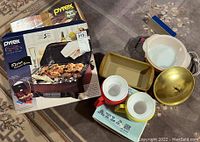 Wide view of Pyrex Portable 5-piece casserole set box and various kitchenware including ceramic bowls and metal lids.
