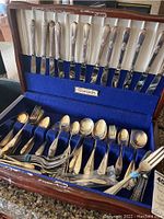 Full view of open wooden anti-tarnish chest containing over 40 pieces of silverplate flatware including knives, forks, and spoons arranged in slots and compartments.