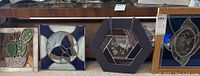 Five pieces of stained glass style wall art displayed side by side on carpet, showing details and variety in designs and frames