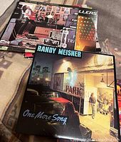 Top view showing Randy Meisner LP record in front, revealing album cover art with a person standing outside illuminated building at night with guitar case and car visible.