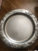 Round silver plate serving tray showing embossed grape and leaf border with plain interior surface