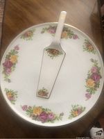 Photo of round cake tray with floral pattern and matching spatula on wooden table.