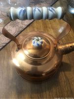 Copper boiling pot with ceramic handle and lid knob on wooden surface