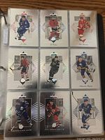 Photo of a binder page holding 9 NHL hockey cards with silver borders and triangular patterns, featuring multiple players and teams.
