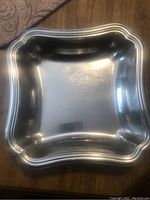 Square stainless steel tray with scalloped edges and decorative border shown on wooden surface.