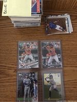 Stack of loose and sleeved baseball cards visible on wood table, with four cards in a binder page at front