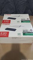 Two sealed Canon E20 cartridge boxes stacked horizontally showing front and side views.