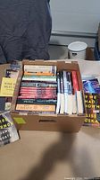 Box containing approximately 35 assorted books, visible titles and mixed genres.