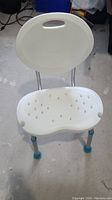 Front and top view of AquaSense height adjustable white shower chair with backrest, showing seat drainage holes and leg rubber tips.