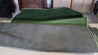Two pieces of artificial grass carpeting displayed with backing side up, showing the stitching and texture of underside and grass pile.