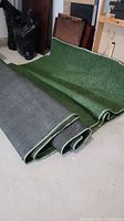 Two folded pieces of green artificial grass carpeting showing texture and back non-slip underside