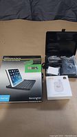 Boxed Kensington KeyCover keyboard case for iPad Air, wireless earbuds box, and battery charging kit close up.