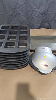 Stack of 8 black rectangular muffin baking trays next to 2 rectangular baking trays and an electric sandwich press seen closed from top.