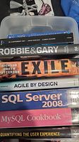 Top view of 8 stacked books showing titles: Wake, In a Different Key, Robbie & Gary, Exile, Agile by Design, SQL Server 2008, MySQL Cookbook, Quantifying the User Experience.