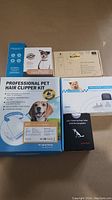 Photo of boxed pet hair clipper kit, dog bark control device box with dog image, LED flashing dog collar box, and pet training collar box arranged on the floor.