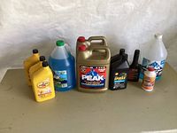 Photo of all automotive fluid containers including motor oil, antifreeze, washer fluid, transmission fluid, brake fluid and additives arranged on flat surface.