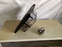 Photo of the black metal 12x12 chimney cap showing the mesh sides and pyramid top, alongside four metal clips.