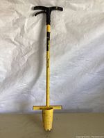 Full front view of the yellow HoundDog bulb planter standing against plain background, showing T-shaped black handle, long shaft, and digging scoop with footrests.