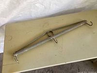 Full view of the metal wire chain link fence stretcher tool lying flat on a beige surface, showing the bar and hooks.