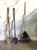 Full view of two shovels and one rake standing upright against a white background.