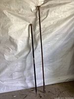 Two long heavy steel garden tools against a white backdrop, the breaker digging bar on the right with pointed and flat ends, and the pry bar on the left with curved and flat ends.