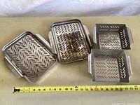 Four stainless steel grill pans arranged flat with measuring tape showing size approximately 12 inches.