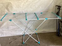 Full view of the metal laundry drying rack standing, showing the multiple metal rods for hanging clothes and blue plastic trim.