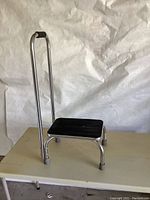 Full view of the step stool showing metal frame, black wooden step, handrail, and rubber foot tips.