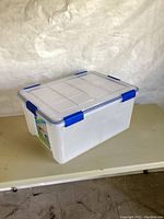 Side view of the white plastic storage tote with blue latches on a beige table.
