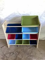 Front view of wooden toy storage rack showing three large and eight small plastic bins in various colors