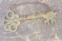Close-up of brass skeleton key-shaped hanger showing detailed bow design and bit section with attached chain.