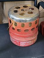 Front view of red Coleman Quick-Lite 30,000 BTU heater showing ventilation holes, metal top, and handle.