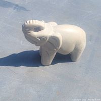 Front angled view of hand carved stone elephant sculpture on gray surface.